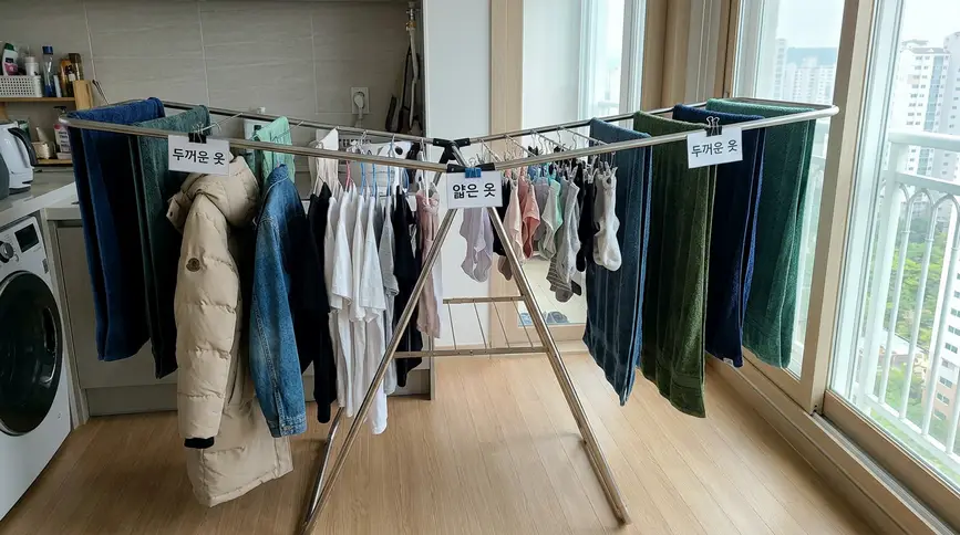 건조대 양 끝에 두꺼운 수건과 긴 코트를 걸고 중앙에 얇은 티셔츠를 배치하여 아래쪽 공기 순환 공간을 확보하는 아치형 배열법
