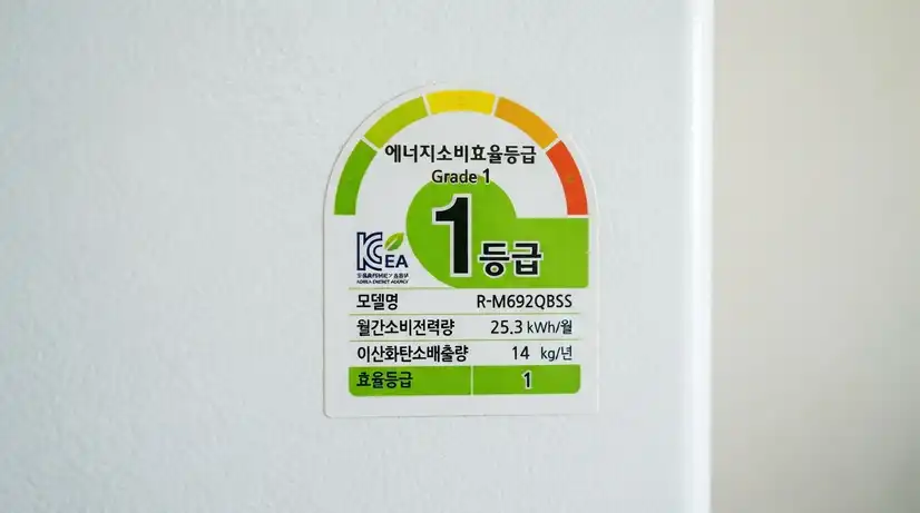 흰색 냉장고 문에 부착된 한국 에너지효율 1등급 라벨 스티커 클로즈업, 녹색 배색의 공식 인증 마크, 선명한 초점 